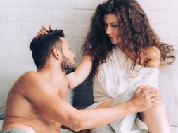 smiling curly woman touching hair of boyfriend in bedroom at home