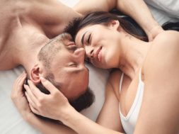 Top view of a smiling sleepy serene dark-haired woman lying in bed with her husband