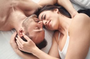 Top view of a smiling sleepy serene dark-haired woman lying in bed with her husband