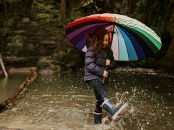 Happy girl playing by the forest lake with an umbrella on a rainy day