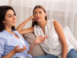 Envy. Jealous Girl Listening To Her Friend Talking About Her Great Life Sitting On Couch At Home. Selective Focus