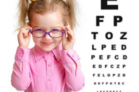 Smiling girl putting on glasses with blurry eye chart behind her isolated on white