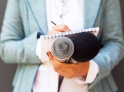 Female reporter at press conference, writing notes, holding microphone