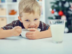 Waiting for Christmas. Little boy eating breakfast on the eve of the new year. Christmas tree in the background.