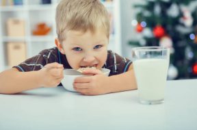 Waiting for Christmas. Little boy eating breakfast on the eve of the new year. Christmas tree in the background.