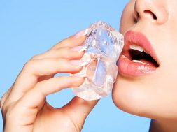 Closeup portrait of beautiful young woman applies the ice to face on a blue background.