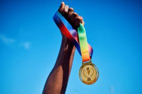 Raised hand holding a gold medal against blue sky. Victory and achievement concept.