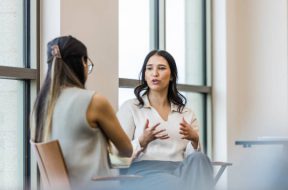 The young adult woman gestures as she details her experience during the interview with the unrecognizable businesswoman.