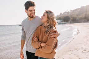 Pleasant young man embracing girlfriend on nature background. Outdoor photo of pleased blonde girl posing at sea with husband.